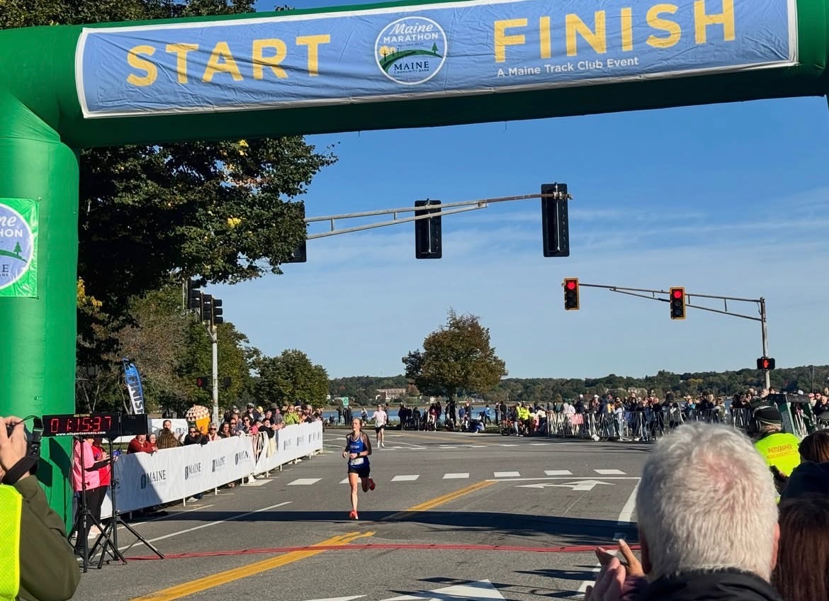A Dirigo runner approaching the half marathon finish beneath the Maine Marathon arch.